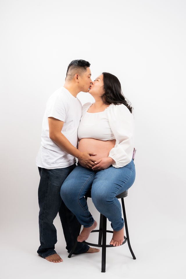 Expecting couple smiling together in a seated studio portrait