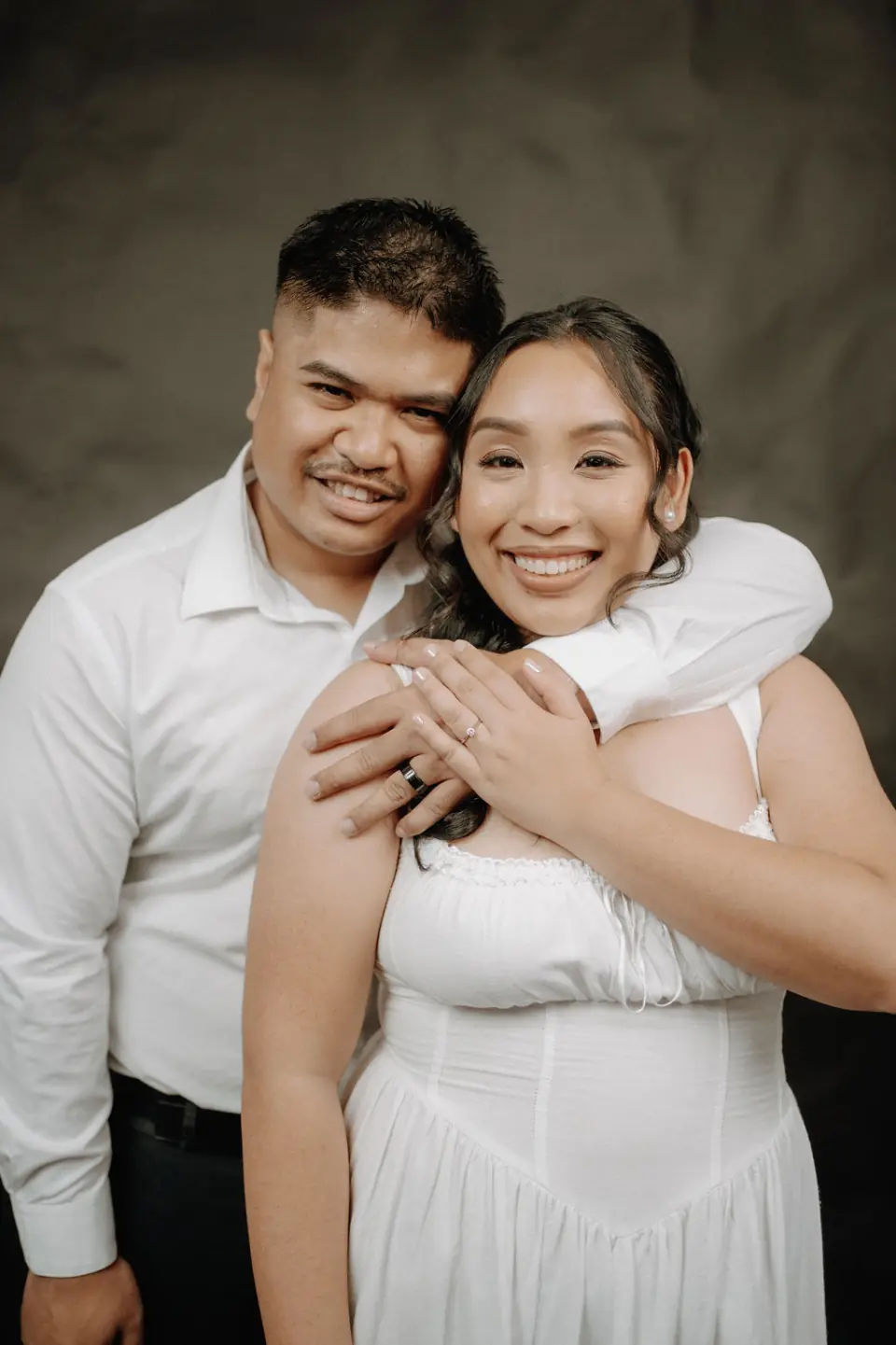Engaged couple embracing against a dark studio backdrop